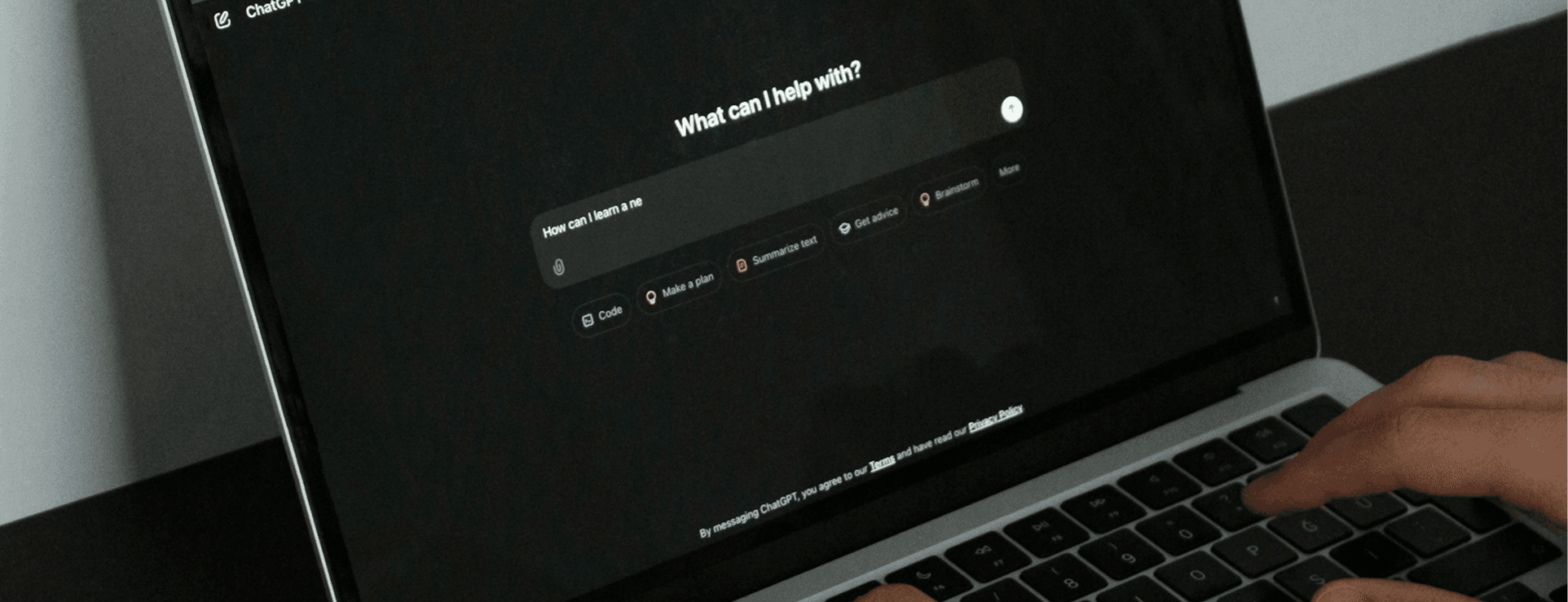 A person sitting in front of a laptop with the screen open to an AI chatbot interface in dark mode. The user is typing on the keyboard.