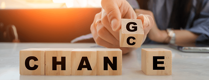 Nahaufnahme einer Hand, die einen Holzwürfel mit den Buchstaben G und C in die Lücke des Wortes CHAN E auf einem Tisch einfügt. Die Würfelreihe buchstabiert das Wort CHANGE, wobei der eingefügte Würfel das Wort CHANCE bilden kann, was symbolisch dafür steht, dass jede Veränderung eine Chance darstellt.