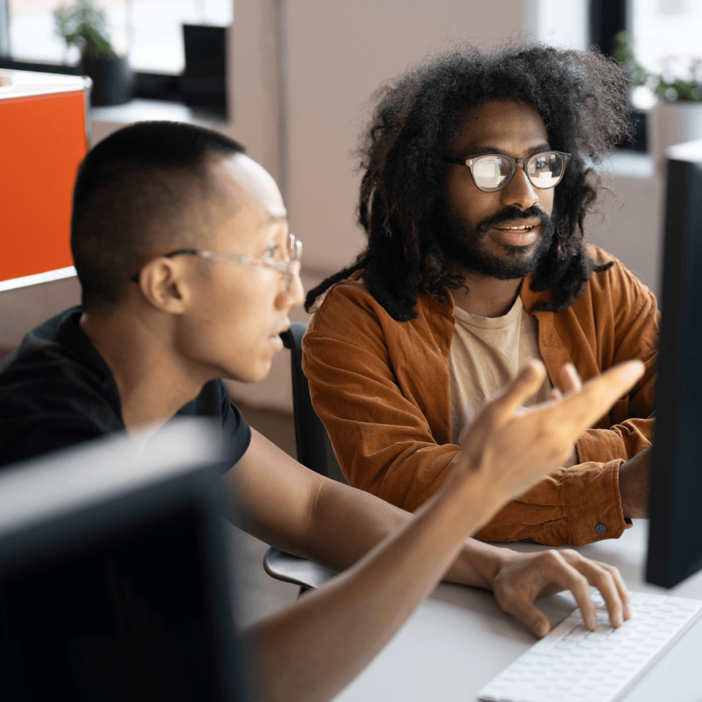 Two colleagues collaborating and discussing work in front of a computer monitor in a modern office setting
